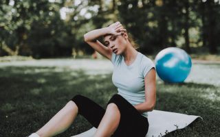 A woman tired from working out sitting down and wiping her forehead