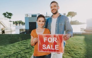 A couple with a "for sale" sign in front of their house