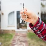 Hand holding a key in front of a house
