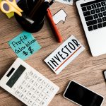 A desk filled with a calculator, laptop, and a piece of paper that says 