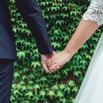 husband and wife holding hands in front of greenery