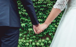 husband and wife holding hands in front of greenery