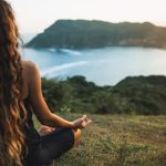 A woman meditating on a mountain top above a body of water