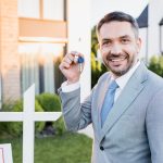 A real estate agent holding keys in front of a house
