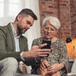 A millennial showing a smartphone to a Baby Boomer