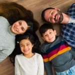 Mother and father and two small children smiling and laying on the floor
