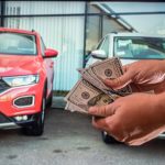A man holding cash in front of used cars on a lot