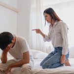 A girlfriend yelling at her boyfriend as they both sit on a bed