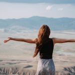female tourist stands in the sun with her arms streched out
