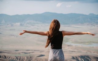 female tourist stands in the sun with her arms streched out