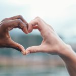 Outdoor, closeup and people with heart sign, hands and support with kindness, emoji and commitment. Outside, couple or interracial with symbol for love