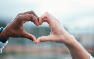 Outdoor, closeup and people with heart sign, hands and support with kindness, emoji and commitment. Outside, couple or interracial with symbol for love