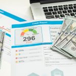 A sheet with 296 credit score and cash near a laptop