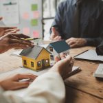 Two model homes on a table with people discussing them