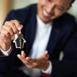A realtor holding up keys and a small model house