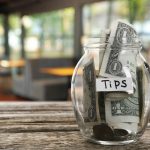 Tips jar with money on wooden table in cafe, space for text