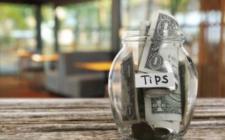 Tips jar with money on wooden table in cafe, space for text