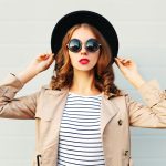A woman with red lips and sunglasses trying on a large black hat