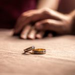 Two wedding rings sitting on a table with hands behind them