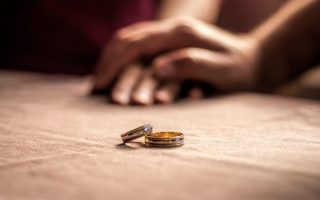 Two wedding rings sitting on a table with hands behind them