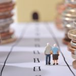A pair of small dolls of elderly people next to stacks of coins
