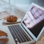 Cropped hand of woman using laptop in cafe