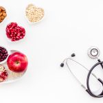 Products good for heart and blood vessels. Vegetables, fruits, nuts in heart shaped bowl near stethoscope on white background top view.
