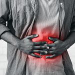 Unrecognizable african american man having stomachache touching aching inflamed abdomen posing on gray wall background indoor. Stomach pain concept. Cropped, black-and-white