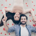 A happy couple laying on the ground holding hands among paper hearts