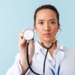 Woman doctor posing isolated over blue wall background with stethoscope.
