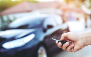 Business man hand holding car keys front with car on background. parking in front of the house.