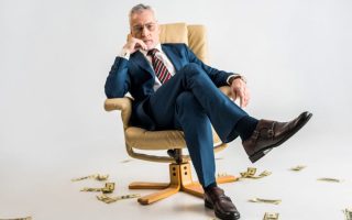 A man with great wealth sitting in a chair while lots of cash lays on the ground around him