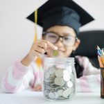 Little girl wearing graduate hat putting coins in jar