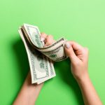 Businesswoman's hands counting one hundred dollar bills on colorful background.