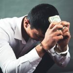 sad man hand in handcuffs holding money