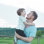 A single parent holding his son in a green field