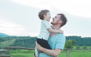A single parent holding his son in a green field