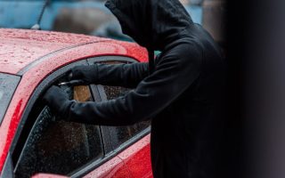 A car thief attempts to break into the window of a red car