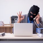 A young male man in a mask attempting to make a computer scam to hurt an older woman