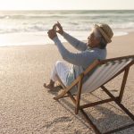 Senior retired woman sitting on the beach taking a photo