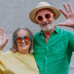 A couple of happy seniors in colourful clothes waving at camera.