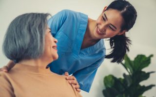 A caregiver resting her hands on the shoulders of a senior patient.
