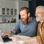 Smiling young man working on a laptop with his senior citizen father