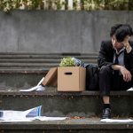 A sad unemployed businessman is sitting on the stairs with a box of his personal stuff