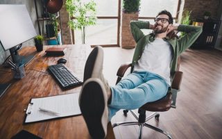 A remote worker at home, smiling and kicking up his feet on his desk