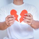 A person holding a broken heart symbol, representing heartbreak or emotional distress.