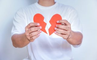 A person holding a broken heart symbol, representing heartbreak or emotional distress.