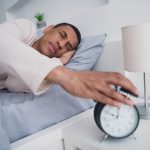 A tired man who didn't get a good night of sleep reaching for his alarm clock