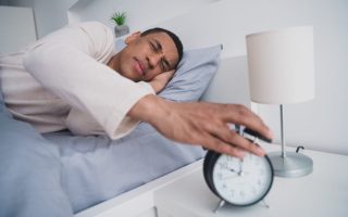 A tired man who didn't get a good night of sleep reaching for his alarm clock
