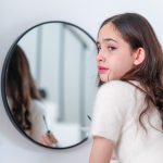 A teenage girl looking away from a mirror